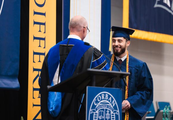 A man in a graduation gown shakes hands with another man, celebrating a significant achievement.