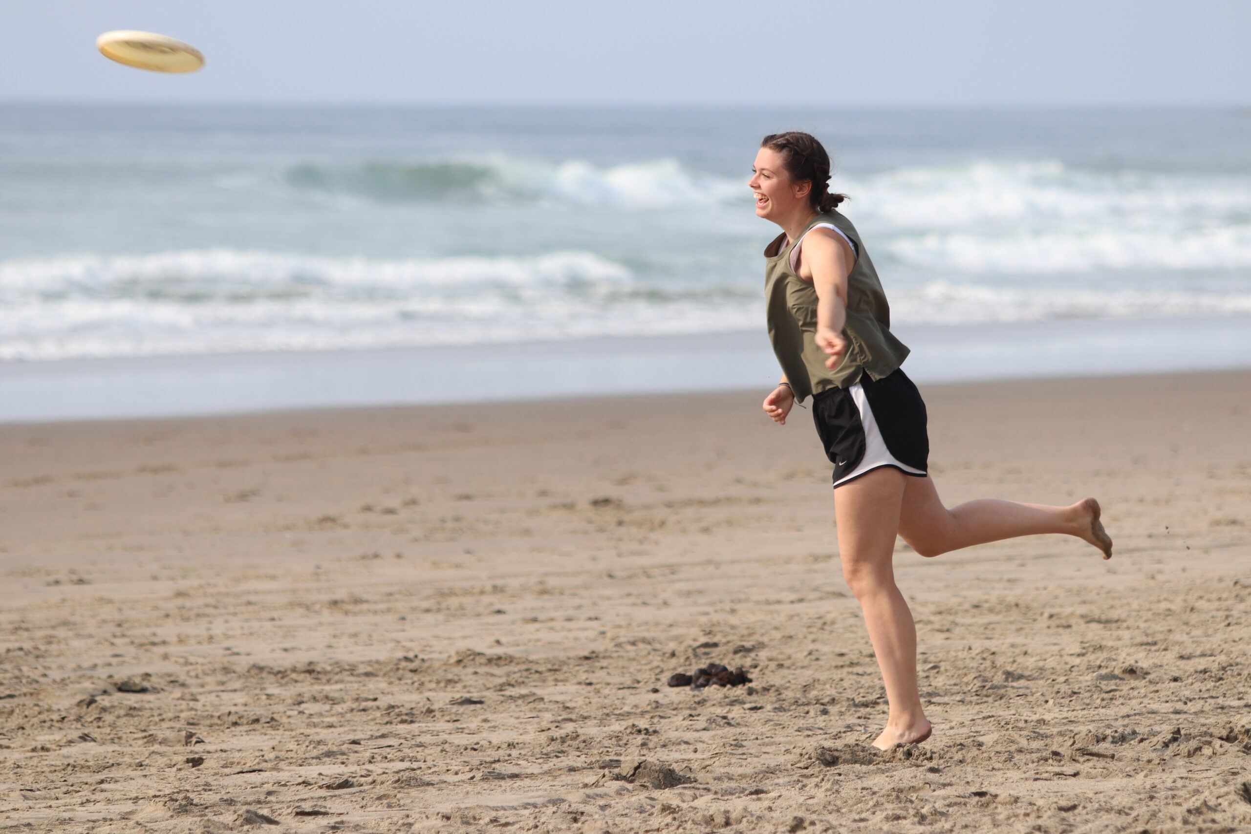 A girl tosses a frisbee on the beach with the ocean behind her