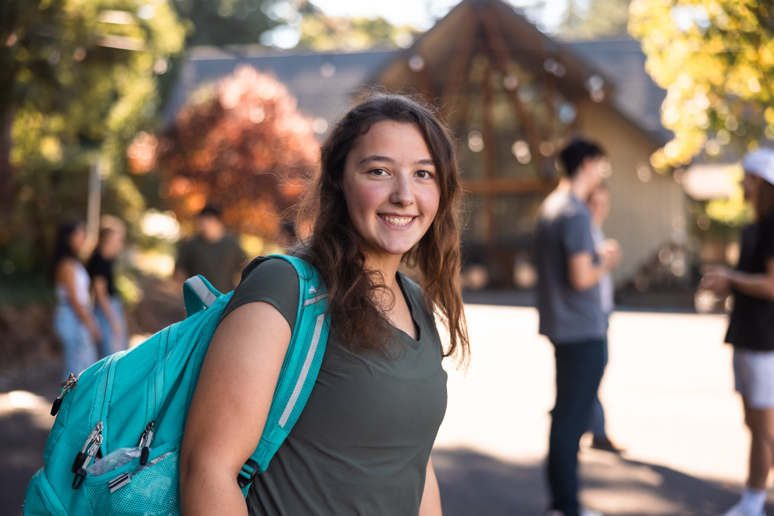 College girl wearing a teal backpack and smiling at the camera in a beautiful outdoor setting