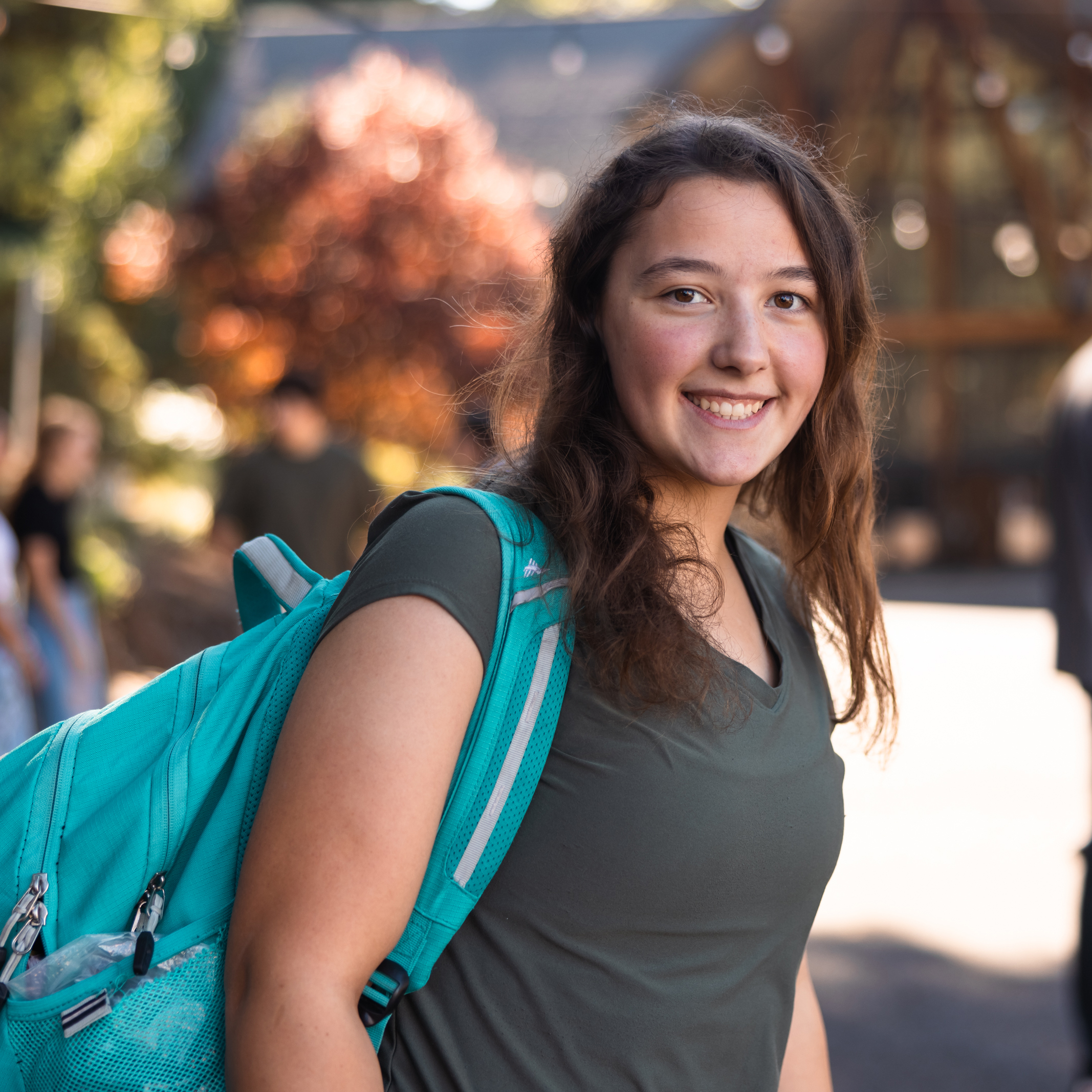 College girl wearing a teal backpack and smiling at the camera in a beautiful outdoor setting