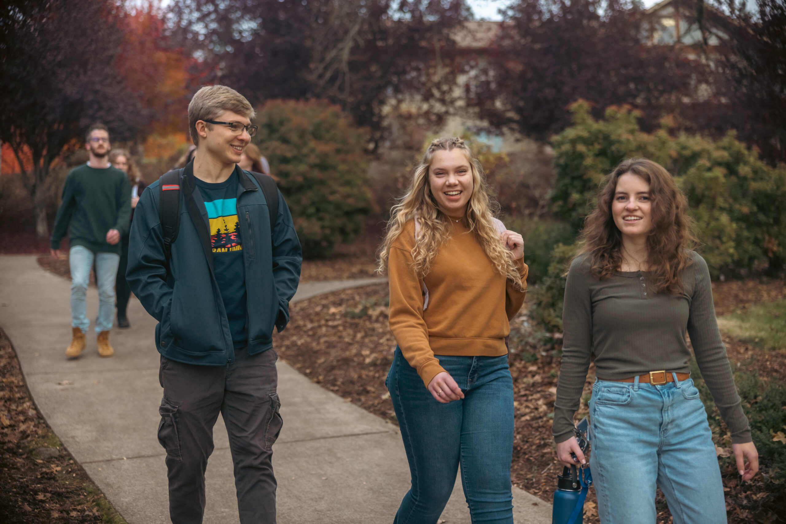 Three students walk together outside talking and smiling.