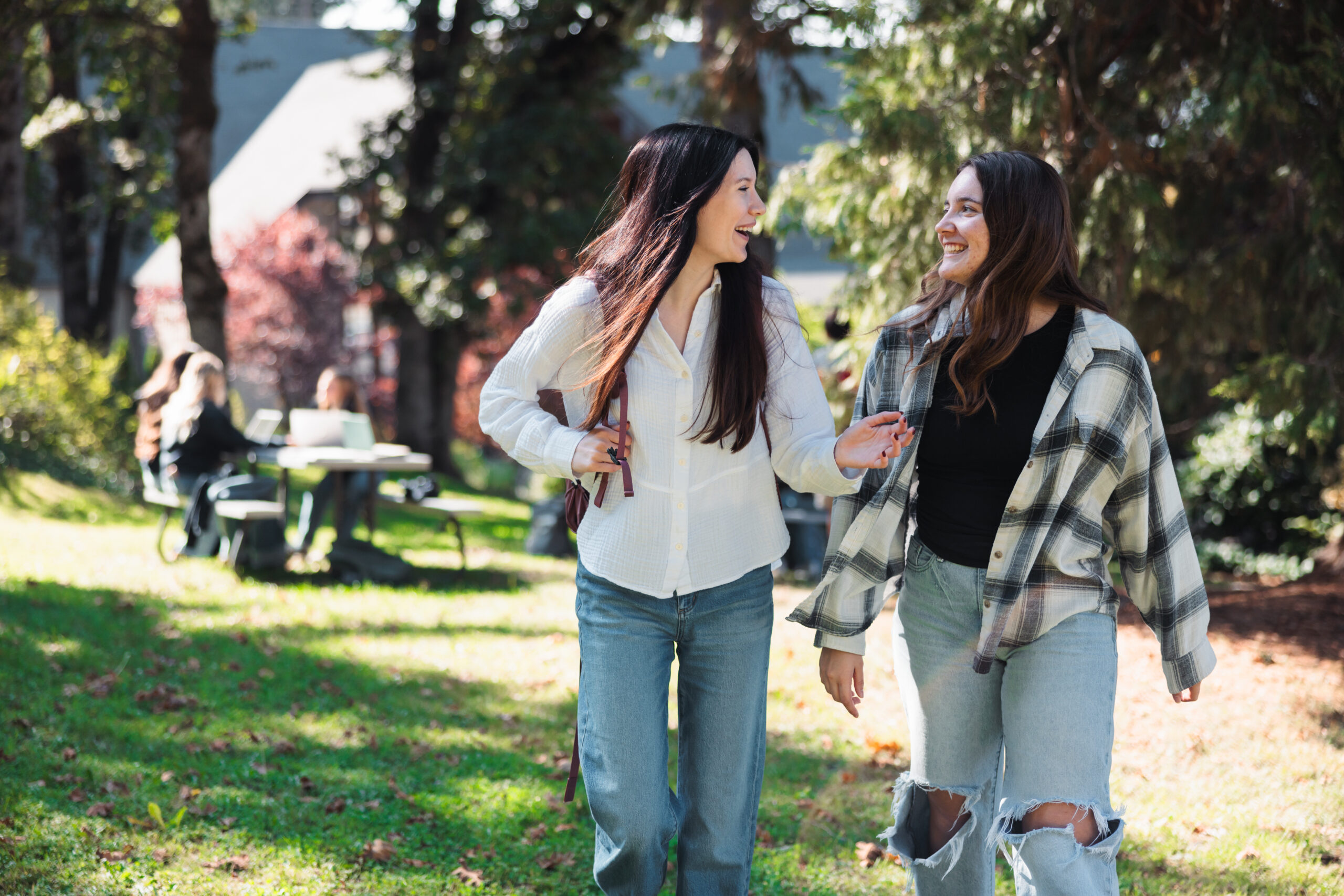 Two women walking side by side in a natural area, enjoying a sunny day and engaging in conversation.