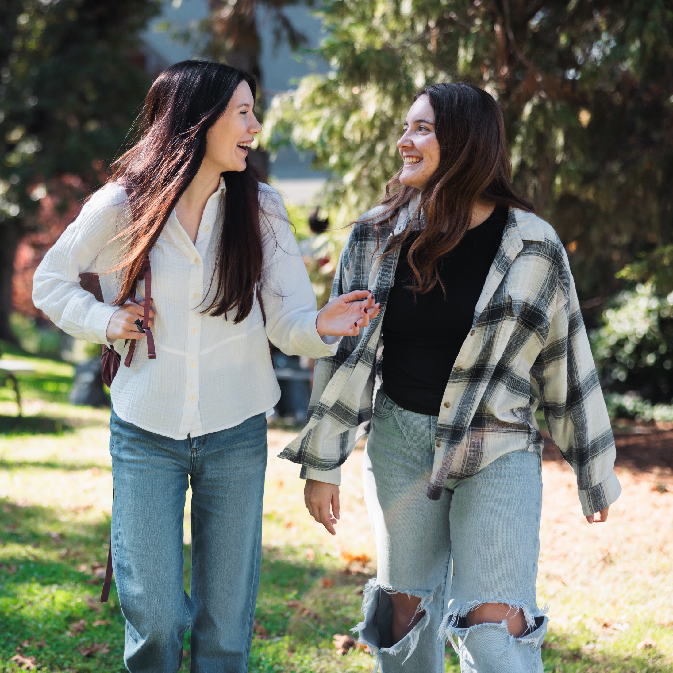 Two women walking side by side in a natural area, enjoying a sunny day and engaging in conversation.