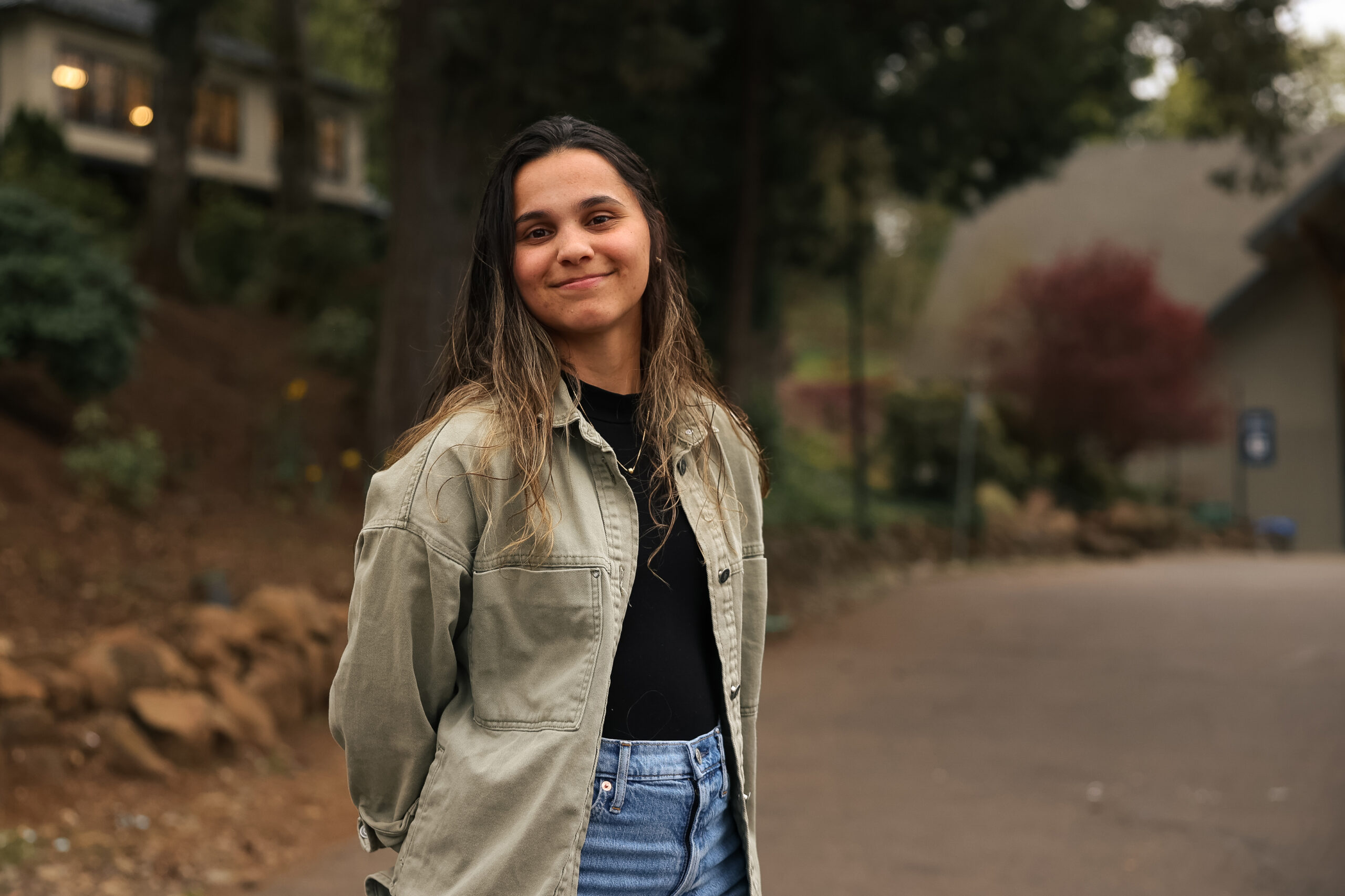 A young woman poses with a smile and her hands clasped behind her back on a college campus