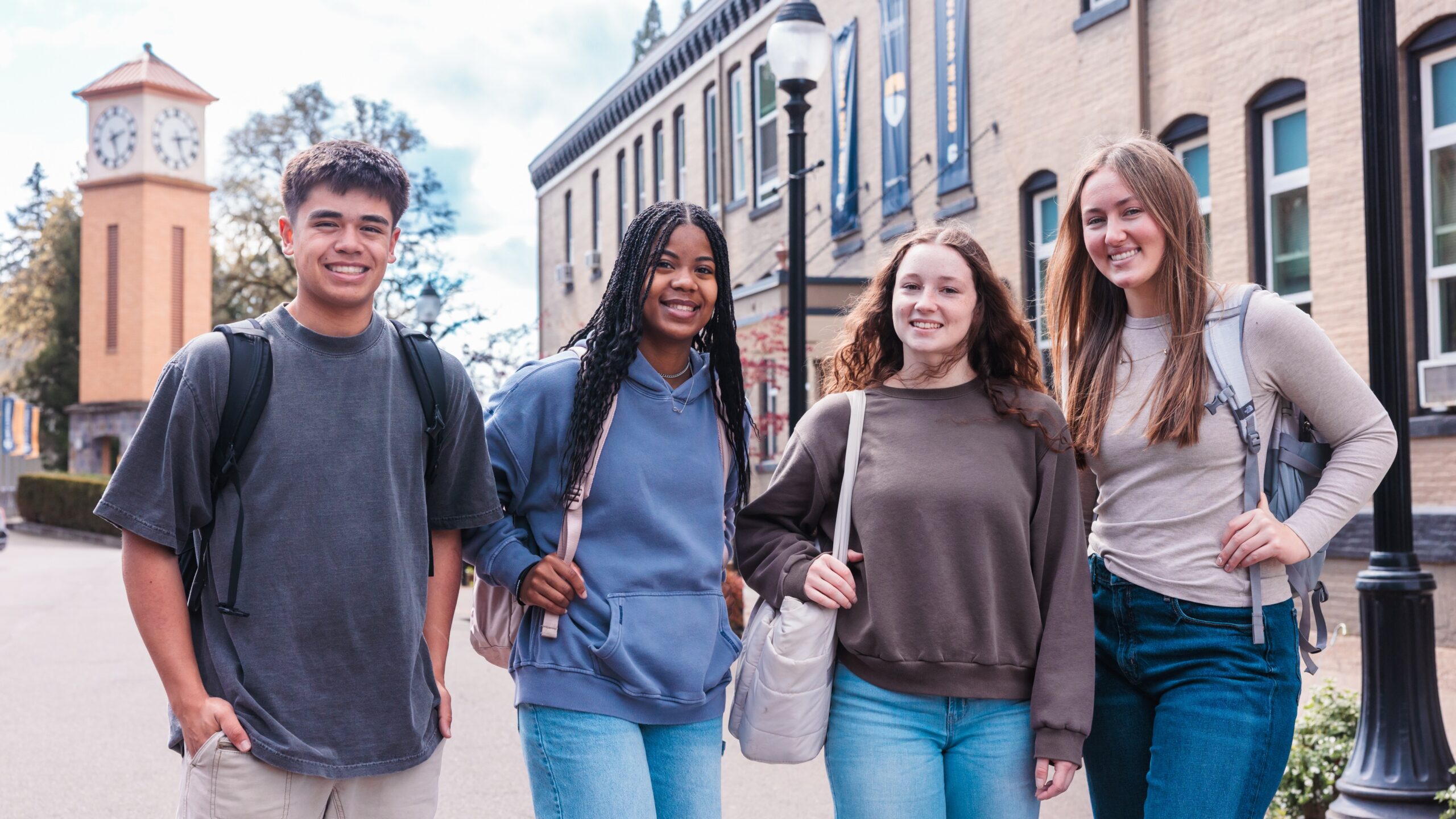 Four young people stand together in front of a stone building, smiling and engaging with each other.