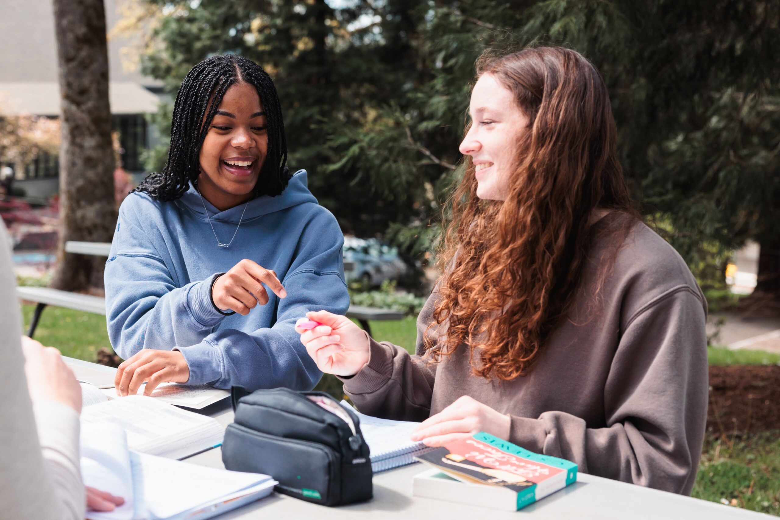 Two students engaged in discussion while sitting at a table, sharing their notes.