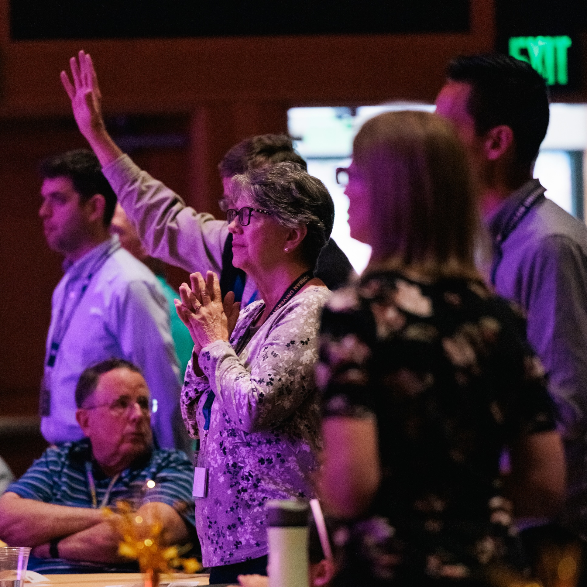A group of alumni at chapel raise their hands reverently in worship.
