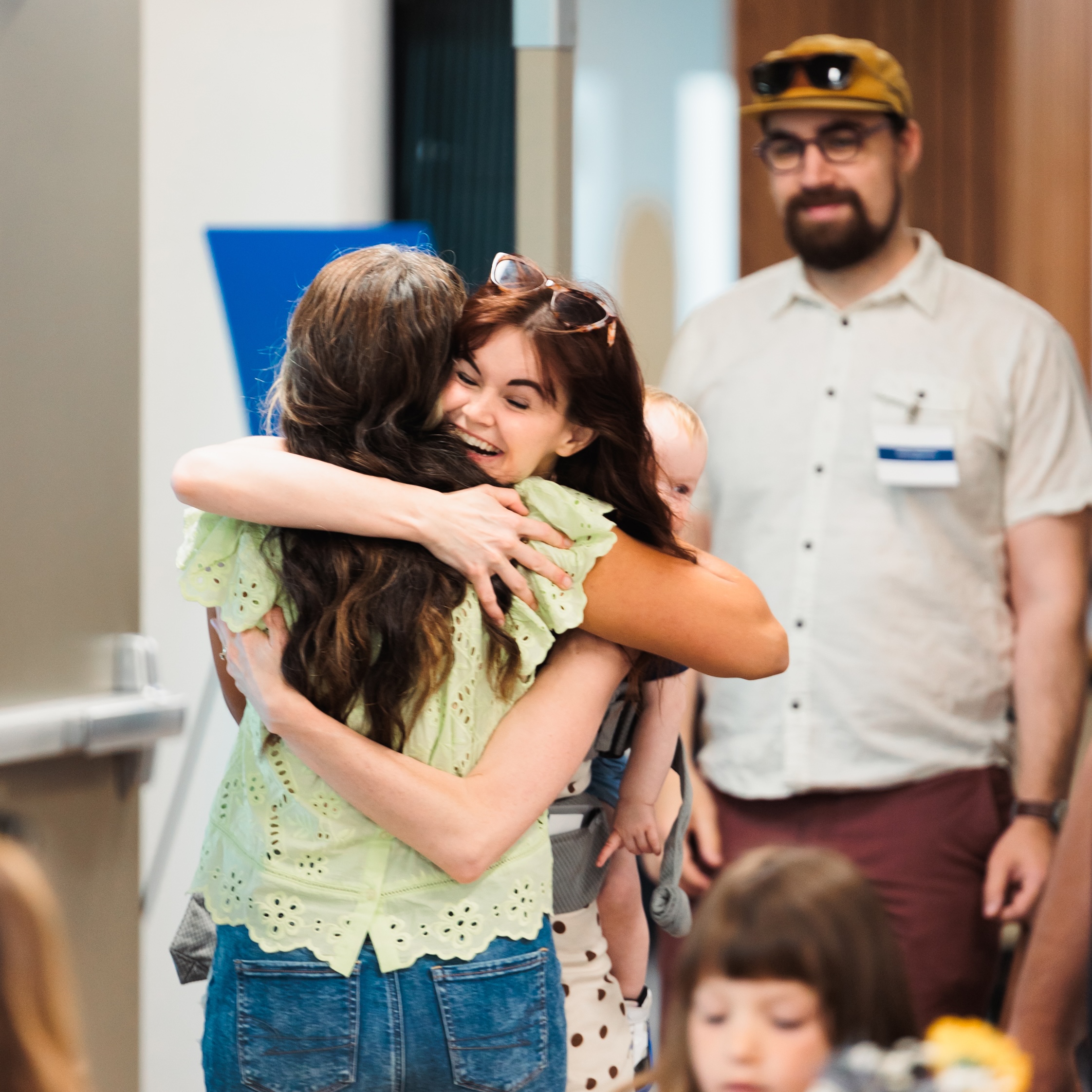 Two women embrace warmly in a crowded room, sharing a moment of joy and connection.