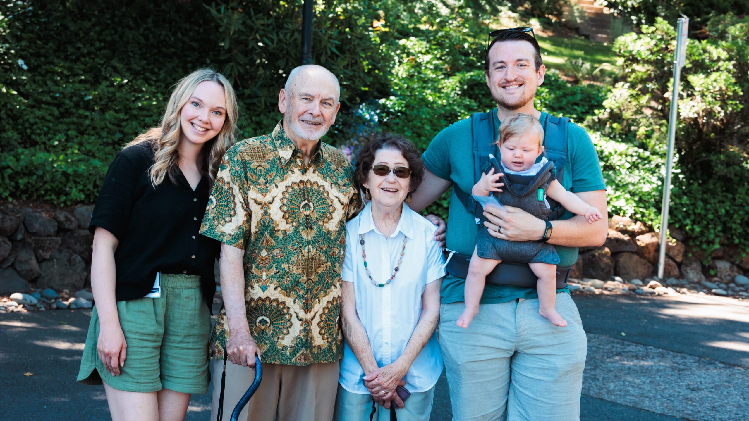 A cheerful family standing together, posing for a picture outdoors with trees in the background.
