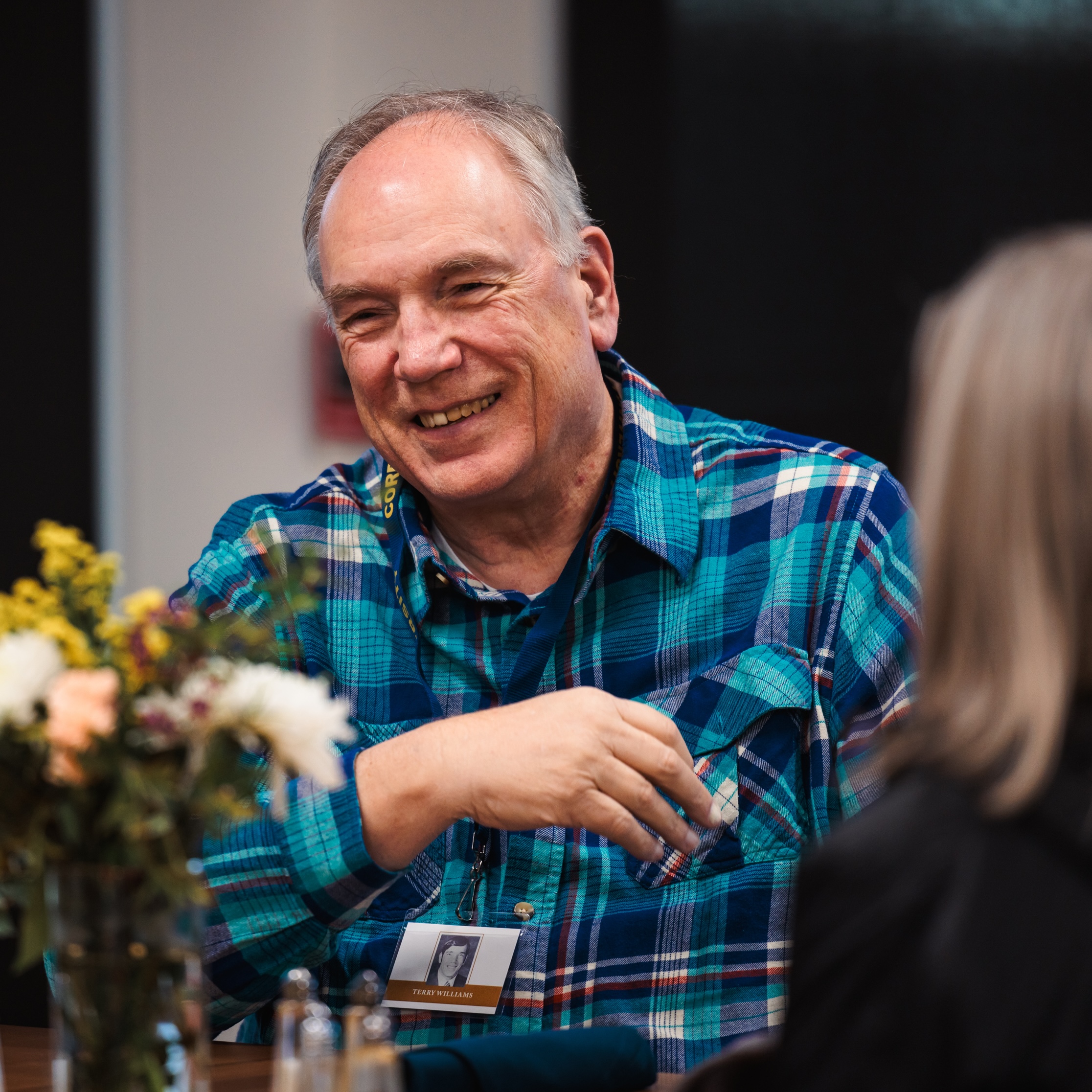A man wearing a blue plaid shirt, engaged in conversation with a smile.