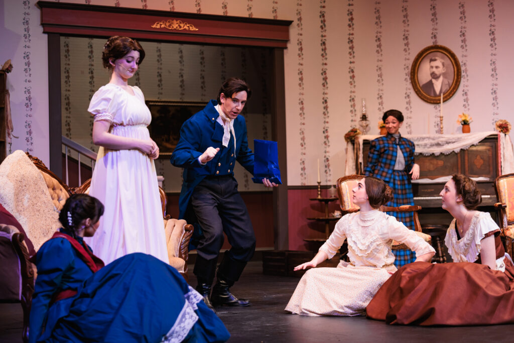 A group of people dressed in period clothing, listening intently to one actor speaking for the play "Good Wives."