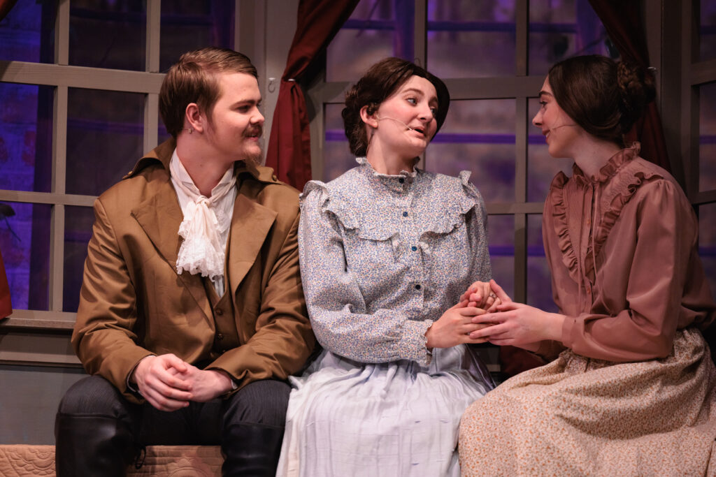 Three actors sitting together on a bench, engaged in conversation for a scene from the play "Good Wives."