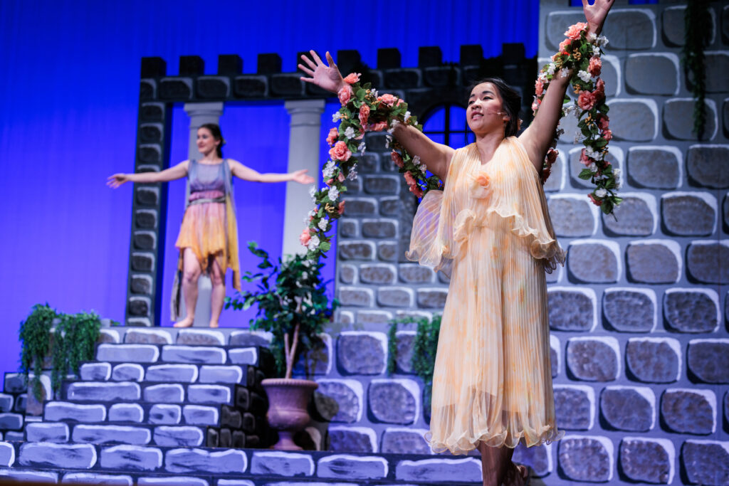 Two woman in dresses stand with arms wide open on stage, representing two fairies in the performance of "Sleeping Beauty, Briar Rose."