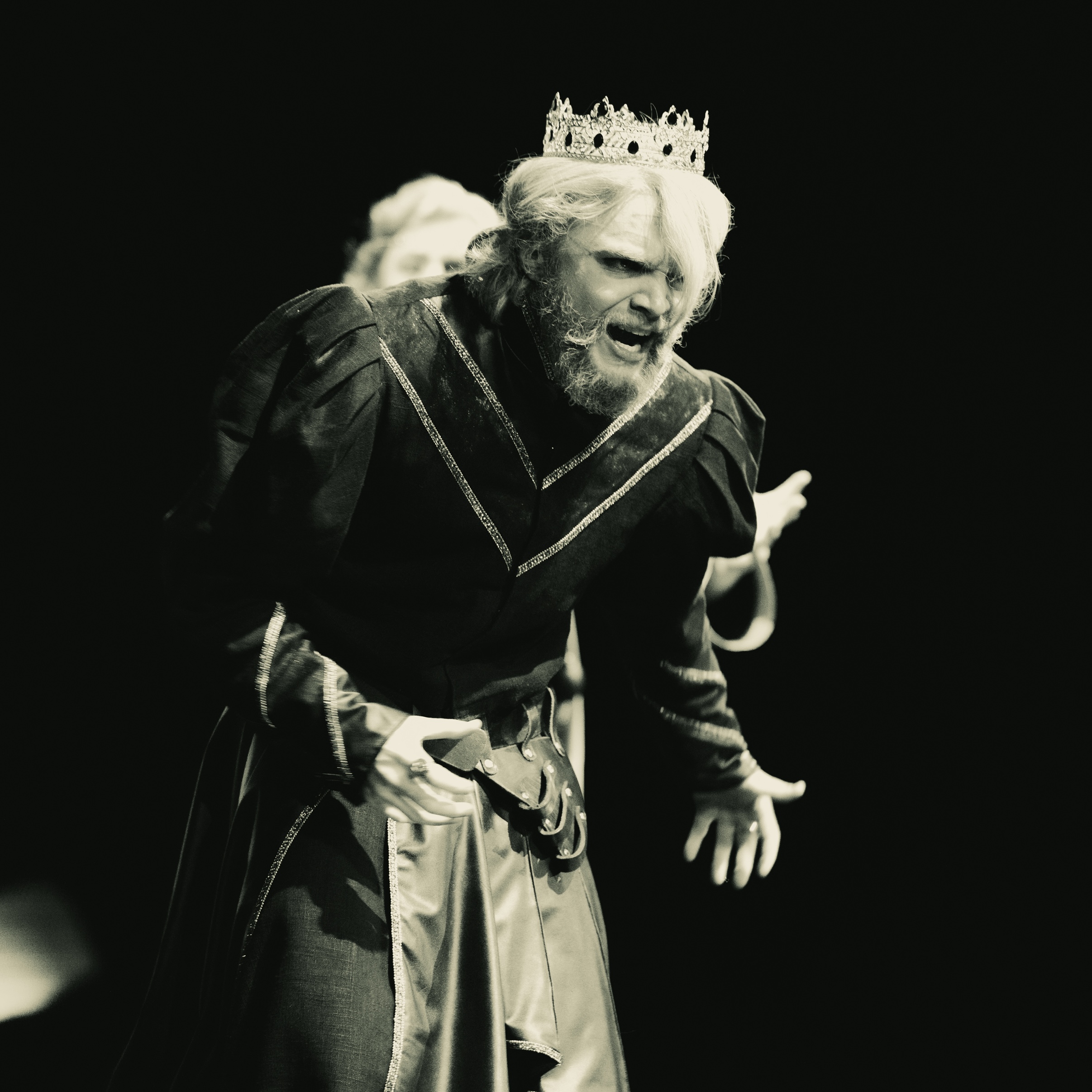 A man dressed in a king's costume with a crown, performing in the "Tragedy of King Saul" theater production.