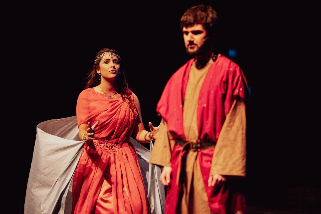 A man and woman in red costumes perform on stage during the "Tragedy of King Saul" play.
