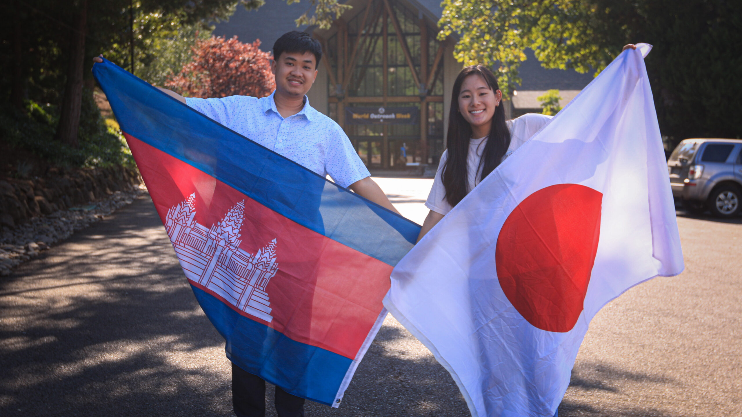 A man and a woman proudly holding flags from their home countries of Cambodia and Japan.