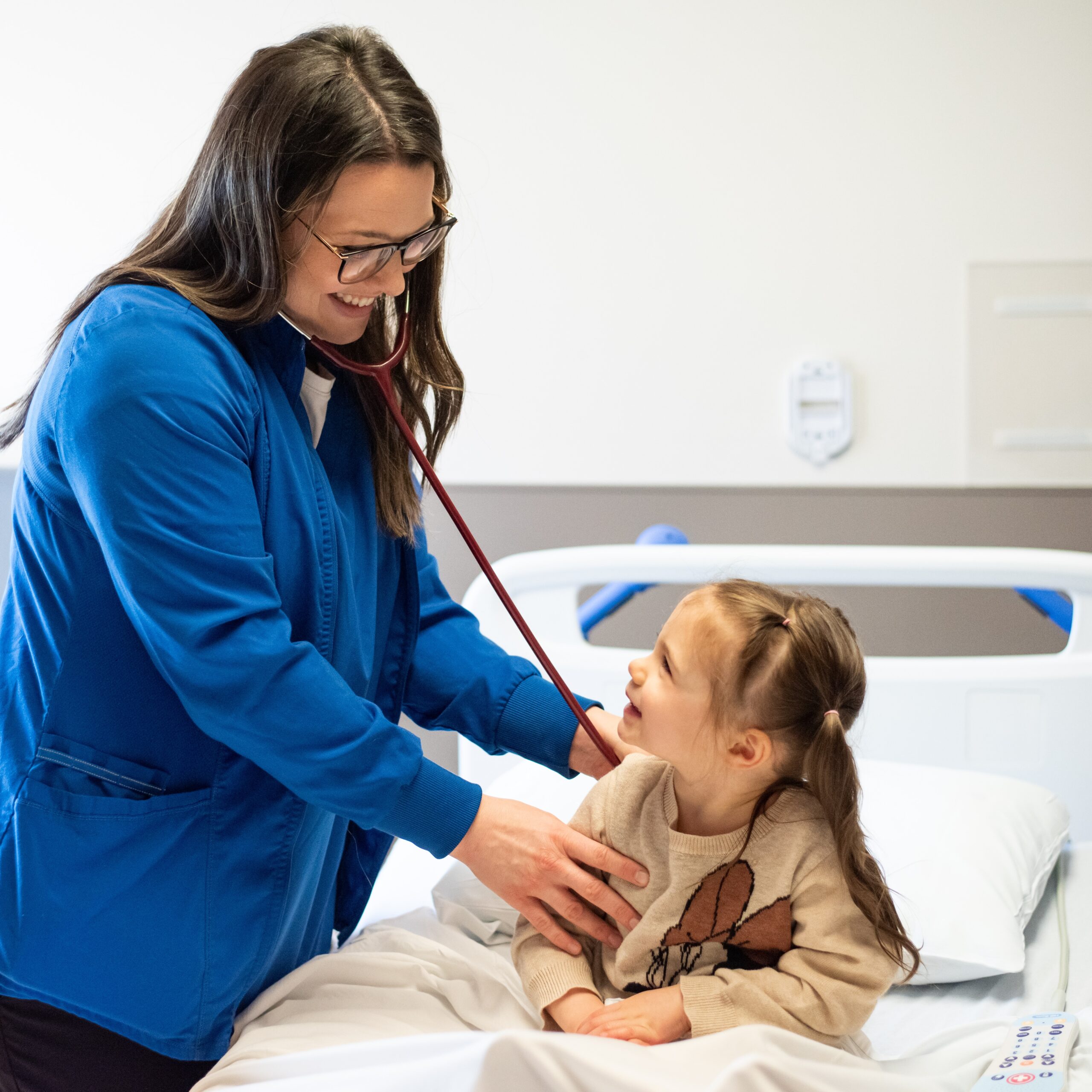 A nurse in blue scrubs is attentively examining a young girl during a medical check-up.