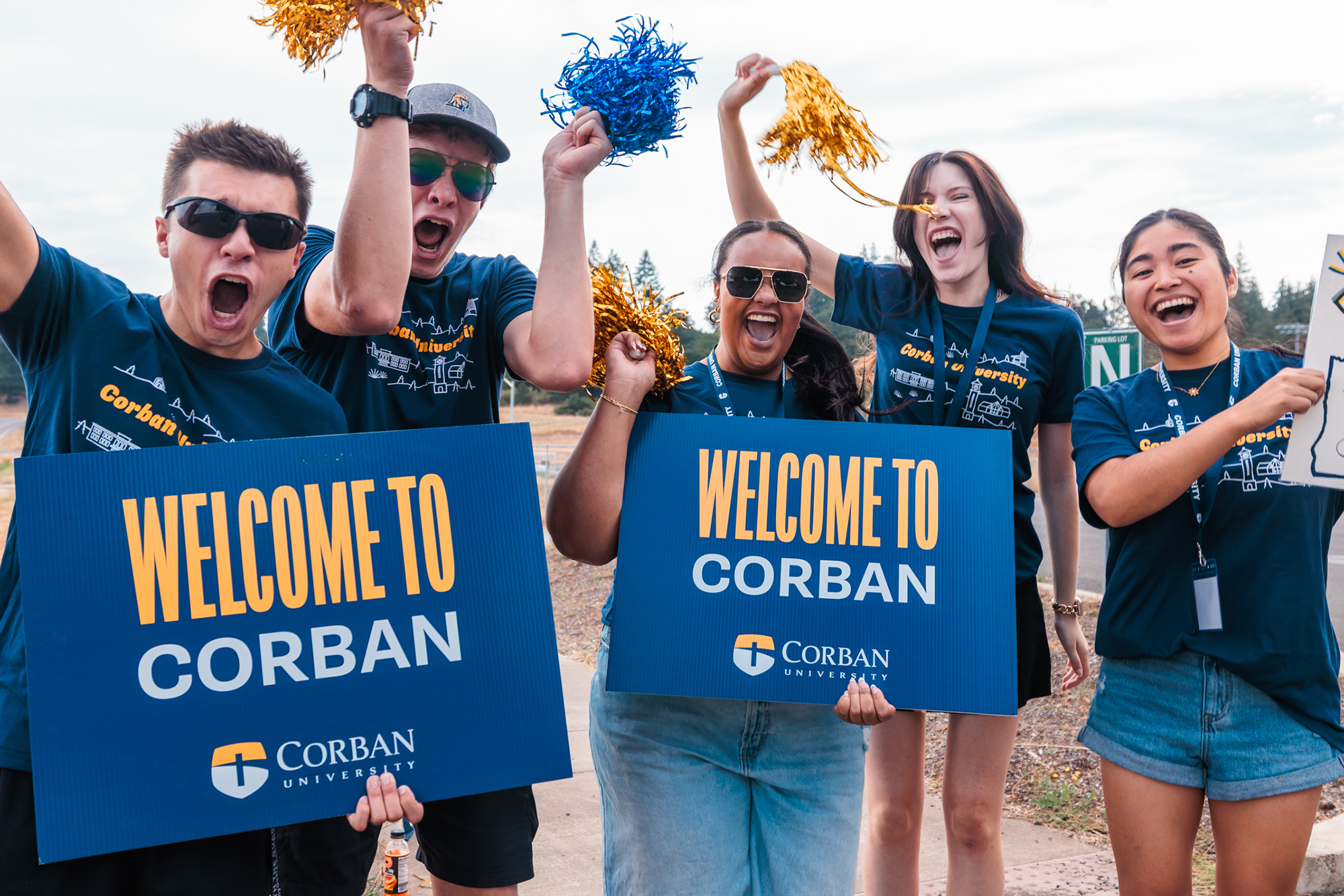 A group of students cheering and holding signs that read "Welcome to Corban" along the roadside during Warrior Welcome.