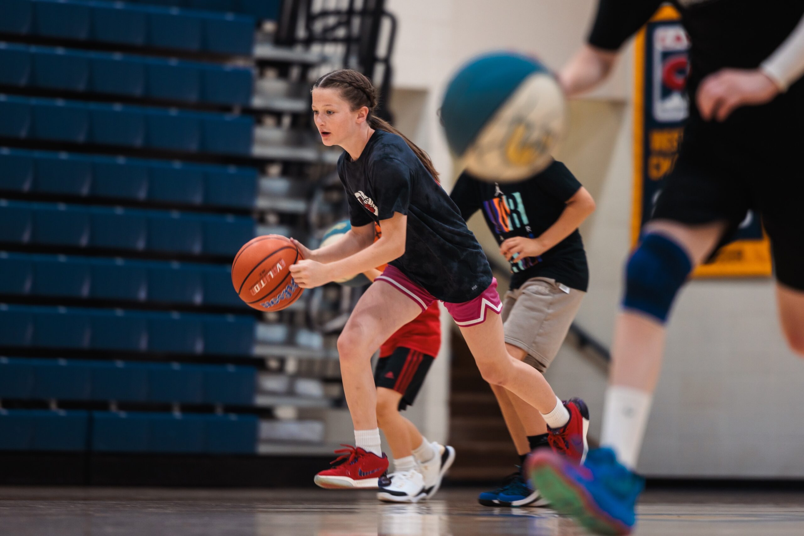 A young girl dribbling a basketball on a court, focused and in motion, showcasing her skills and enthusiasm for the game.