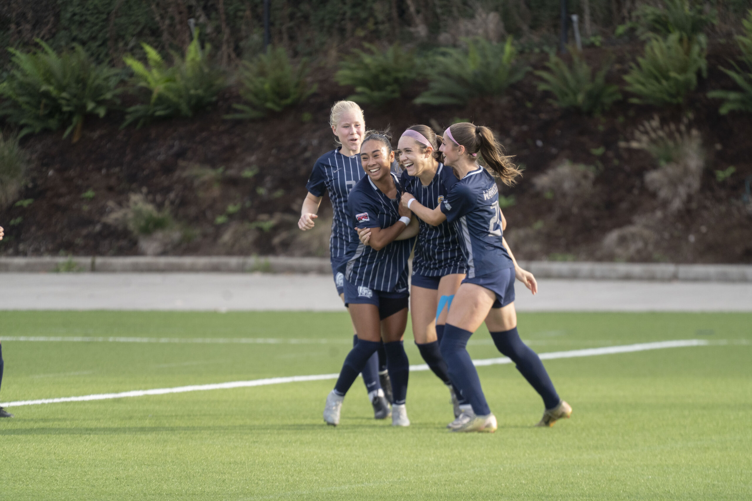 Women's soccer team joyfully celebrates together after scoring a goal on the field.