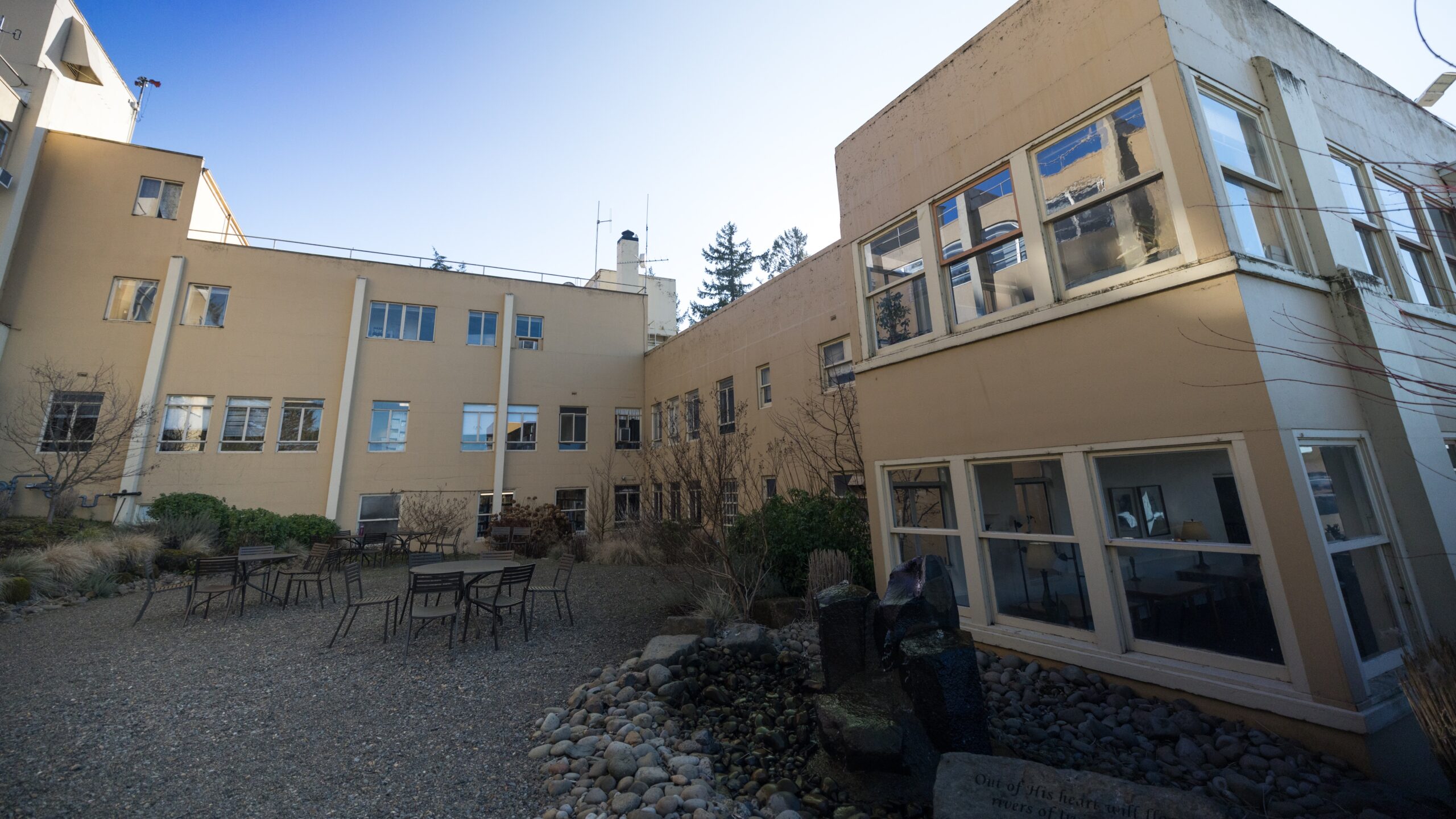 An outdoor gravel area with tables surrounded by the Academic Center, known as the Academic Center Terrace.