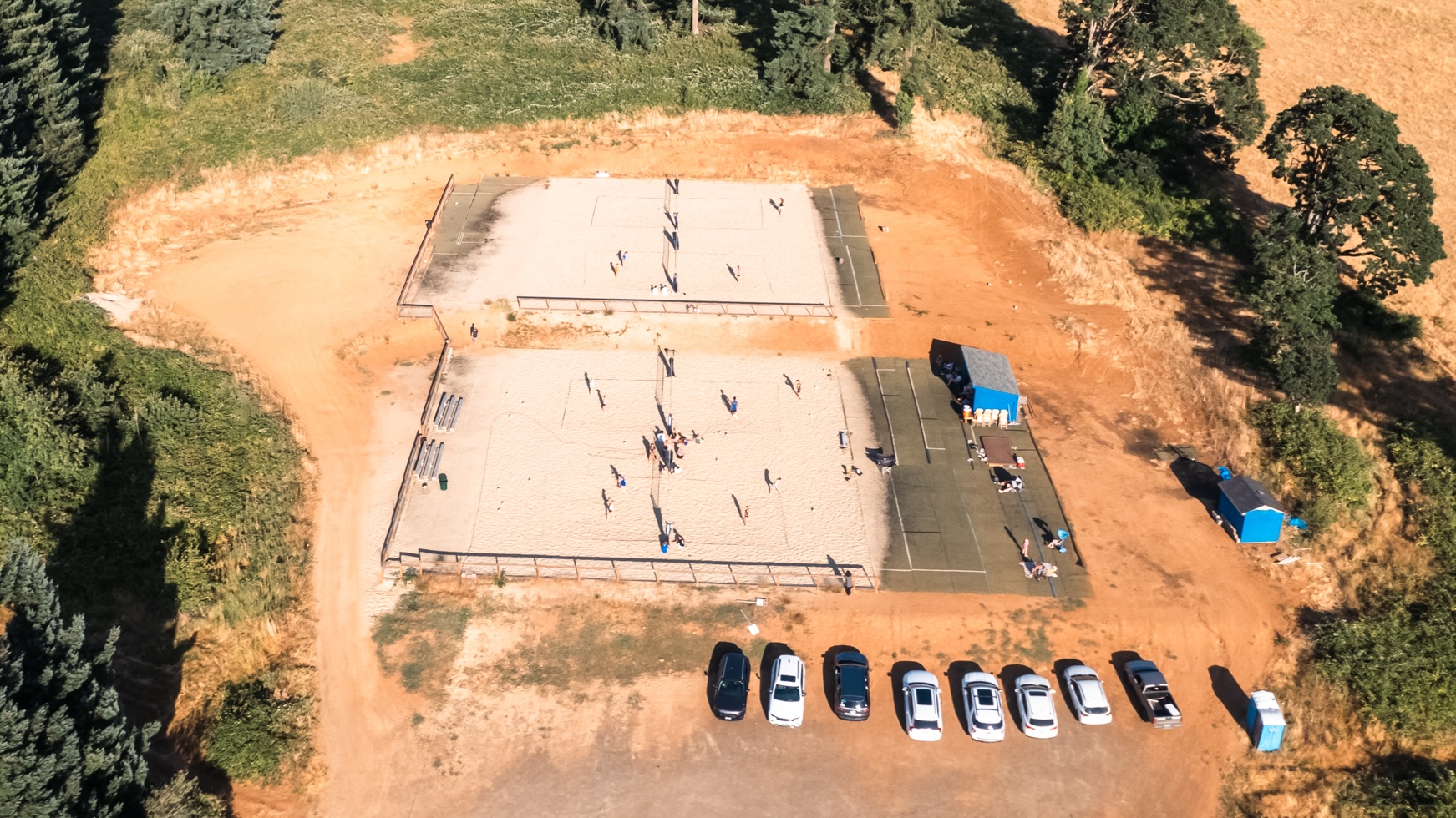 Aerial view of beach volleyball courts with parked cars.