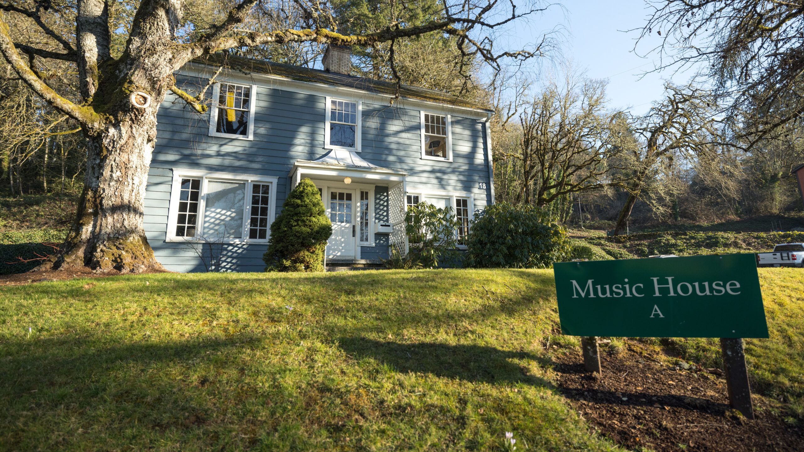 A blue two-story house on a sunny day, surrounded by trees and a lawn. A sign that reads "Music House A"