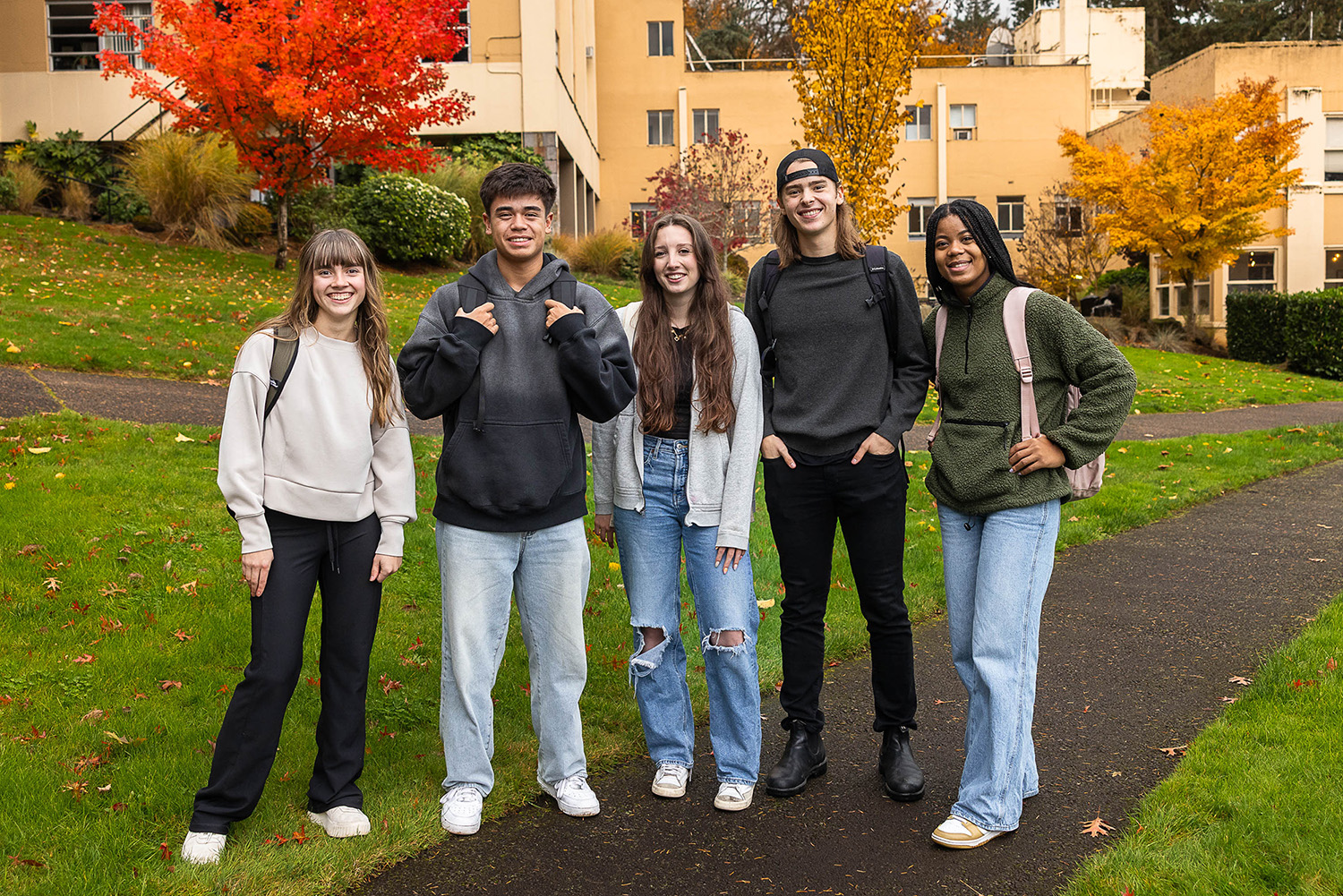 Five young adults gather in front of a campus building, sharing smiles and a moment together.