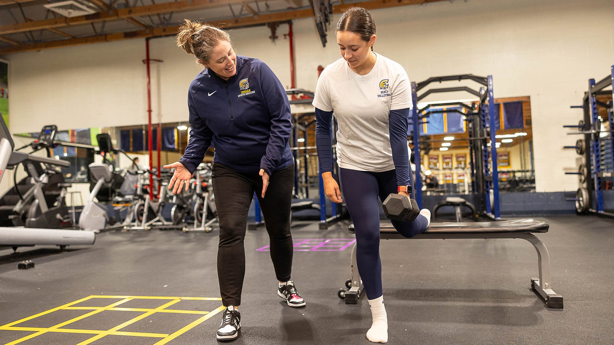 An athletic trainer guides an athlete through strength and conditioning workouts in a gym setting.