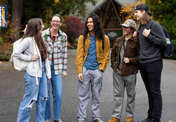 Five young people stand together smiling in front of a modern building.