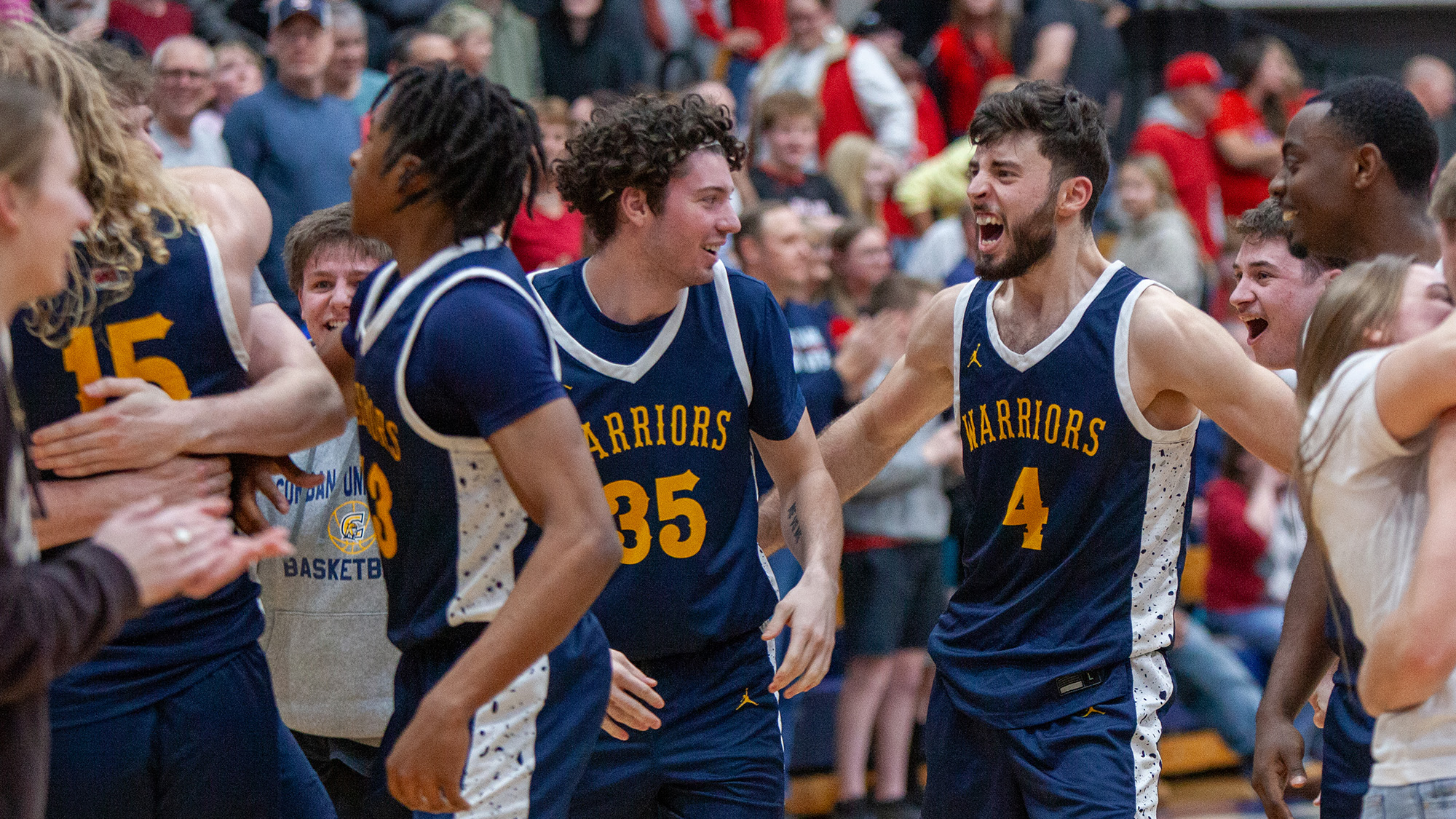 The men's basketball team celebrates joyfully after their hard-fought victory, high-fiving and cheering together.