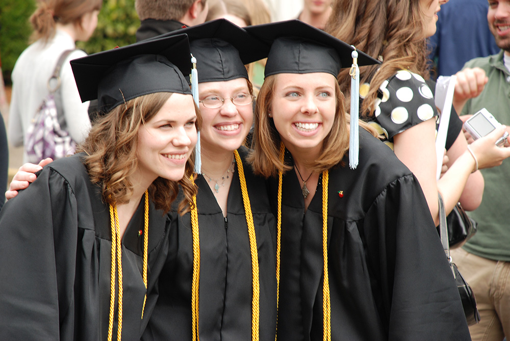 Three women in caps and gowns, joyfully posing for a photo after their college graduation ceremony.