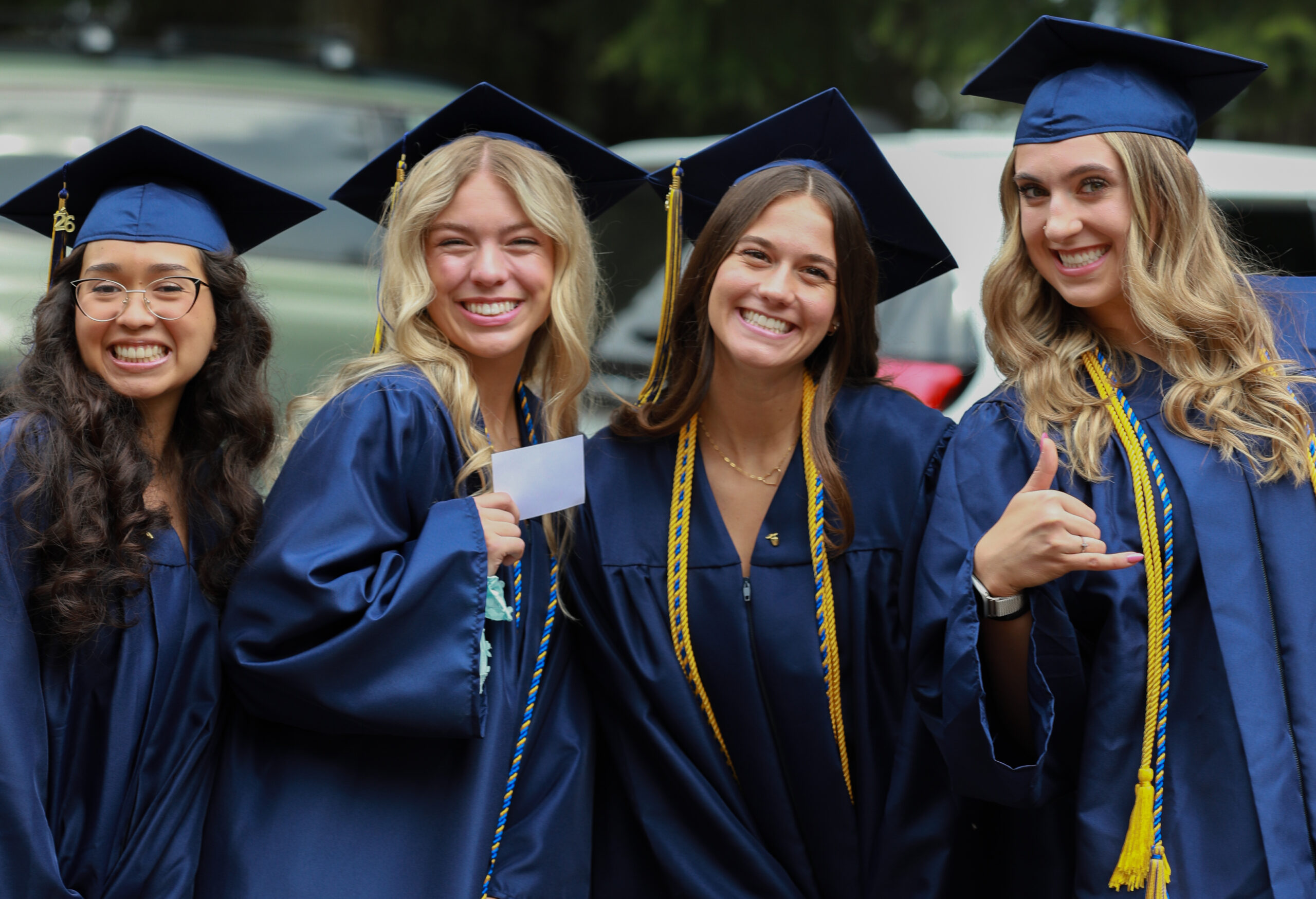 Four young women in blue graduation gowns and caps pose for a photo at Commencement 2026