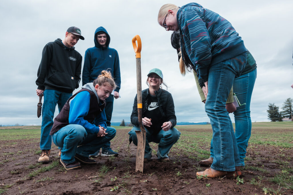 Corban University agriculture science students gather in a farm field to conduct soil sampling and evaluate field conditions during a hands-on learning experience with a local agricultural partner.