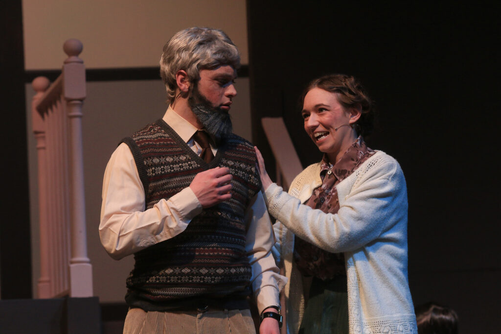 A woman places her hand on a man's shoulder and shares a happy moment in a scene from The Hiding Place play