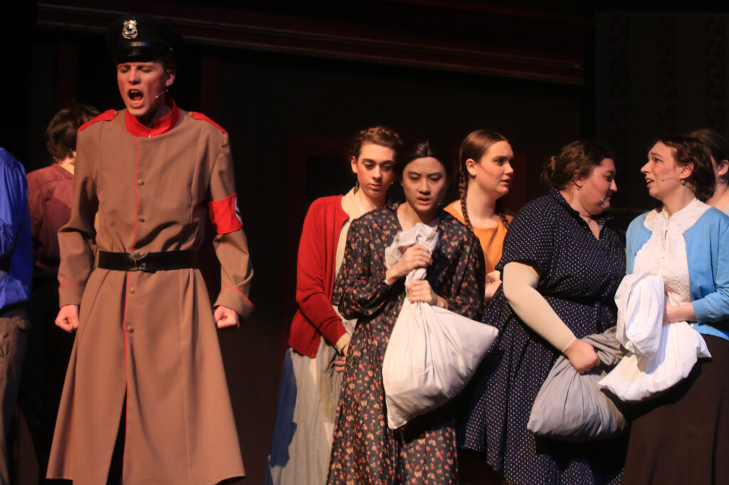 scared women grip pillowcases with their belongings while a soldier yells in a scene from The Hiding Place play