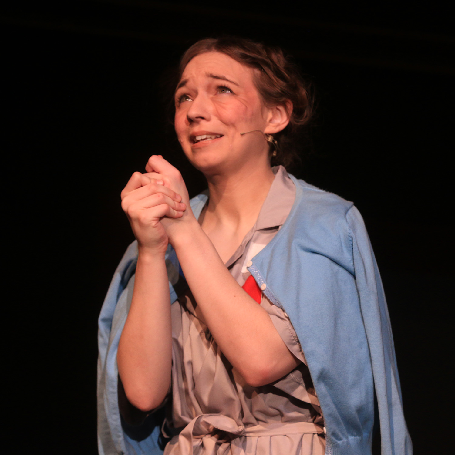 A young woman kneels and clasps her hands in pleading prayer as she portrays Corrie Ten Boom in the play "The Hiding Place"