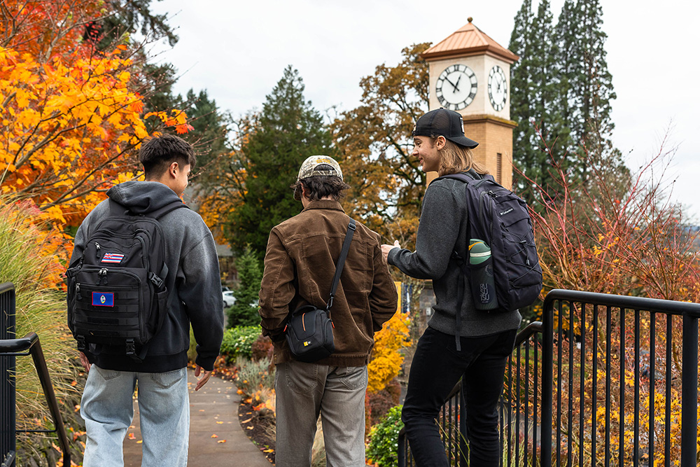 Three guys wearing backpacks walk to class on campus in the fall