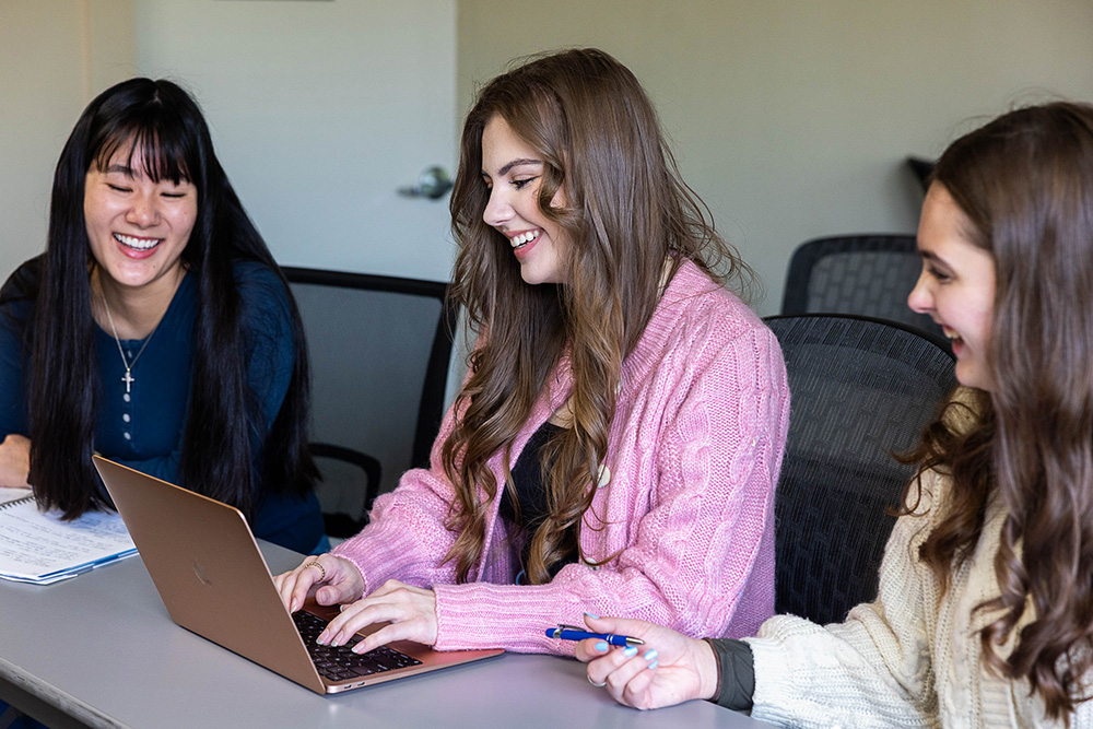 Three female students in a classroom, working on a laptop