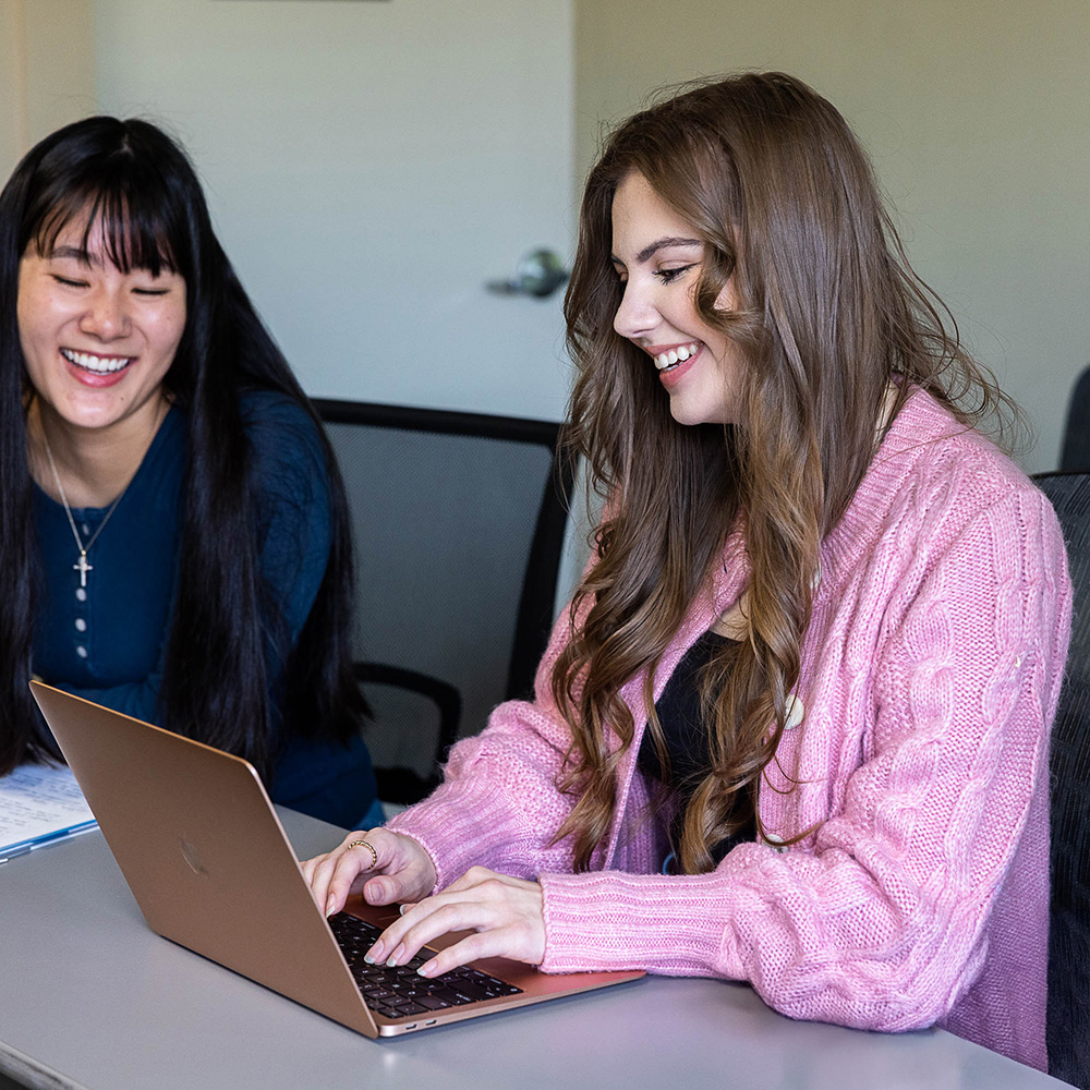 Two female students in a classroom, working on a laptop